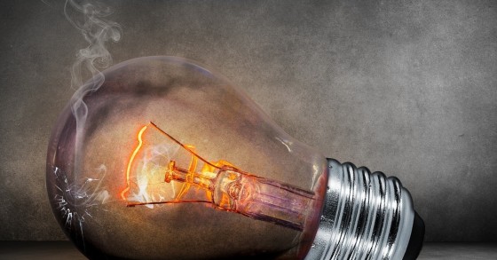L'immagine in primo piano di una lampadina elettrica con luce gialla all'interno su sfondo scuro