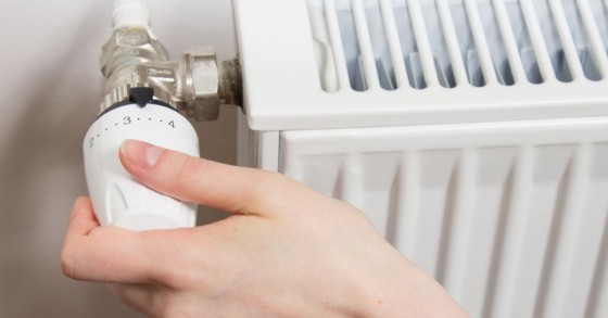 Mano di una persona intenta a ruotare o regolare una moderna valvola termostatica installata su un termosifone