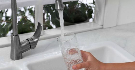 Persona che fa scorrere l'acqua dal rubinetto di casa bicchiere