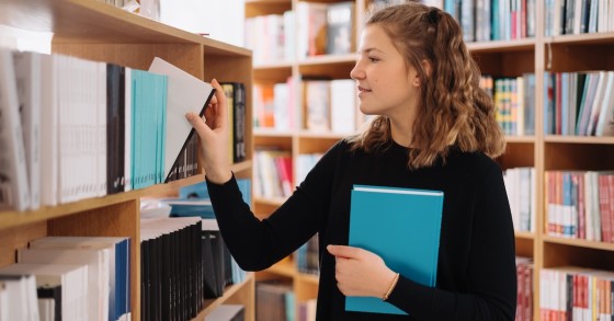 Giovane sceglie un libro dallo scaffale della biblioteca