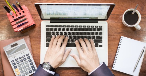 Vista dall'alto delle mani di un uomo d'affari al lavoro su laptop e tablet su una scrivania in legno