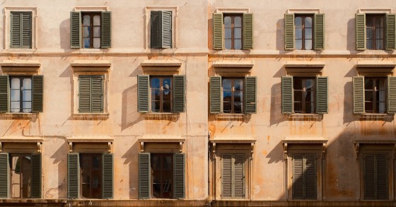 Elegante facciata di un edificio storico con finestre con persiane che proiettano ombre nella calda luce del sole.