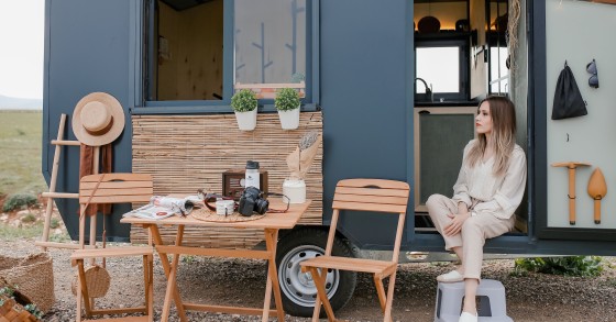 Una donna che si rilassa fuori dalla sua moderna tiny house mobile in un ambiente naturale panoramico.