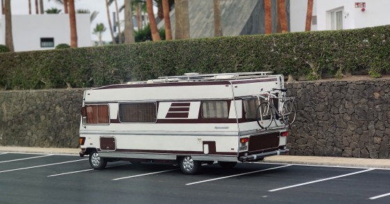 Un camper d'epoca parcheggiato all'aperto vicino a un edificio moderno con palme, a suggerire un mix di avventura e relax.