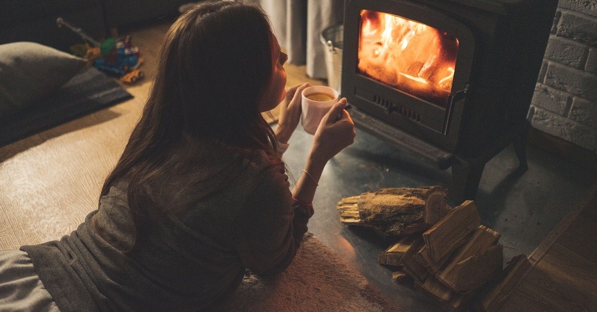 Una ragazza sdraiata davanti ad una stufa a legna accesa