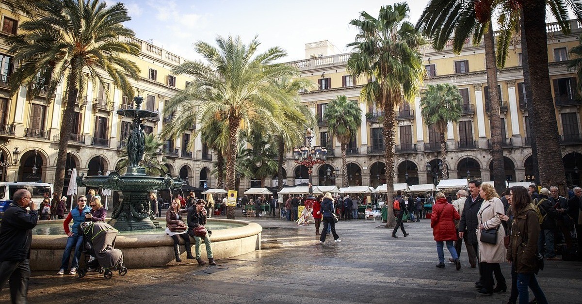 Una piazza dalla pianta quadrata di Barcellona circondata da alberi ed una fontana al centro