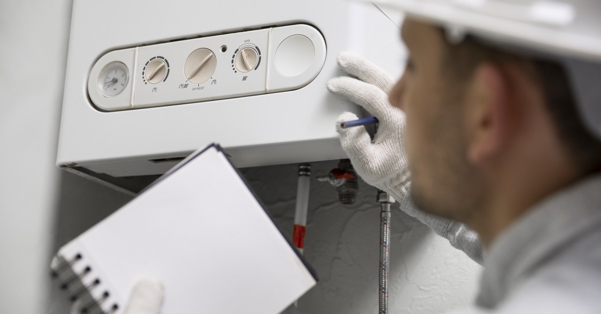 Un tecnico con camice e guanti bianchi che controlla una caldaia