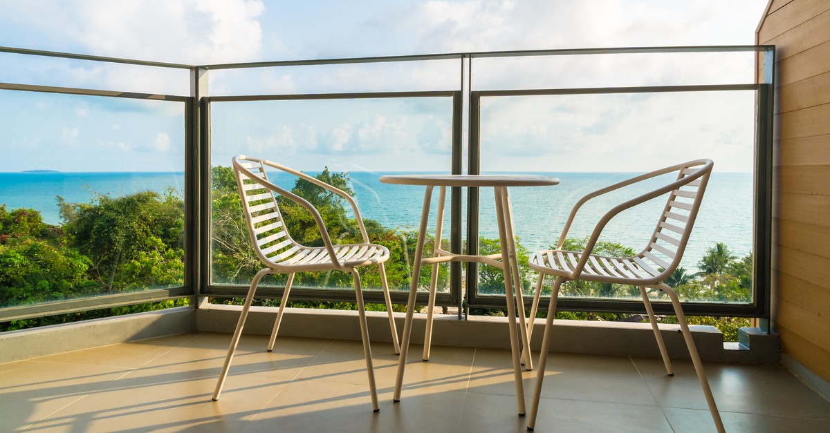 Un balcone con pareti in vetro, un tavolo e due sedie