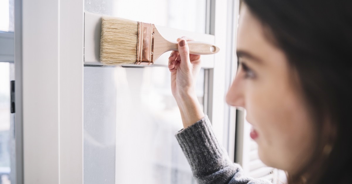 Una donna ridipinge gli infissi di una finestra Una donna ridipinge gli infissi di una finestra