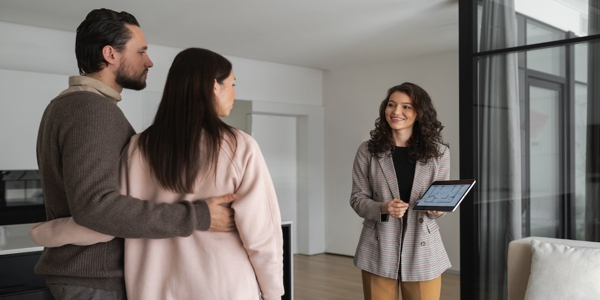 Differenza tra prezzo e valore di un immobile: quanto incide sulla vendita? Agente immobiliare mostra immobile a una giovane coppia
