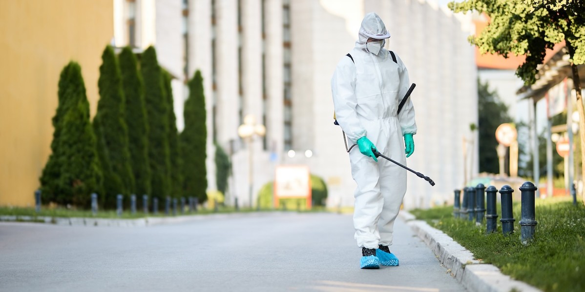Operatore in tuta bianca di protezione chimica che disinfetta vialetti e aiuole 