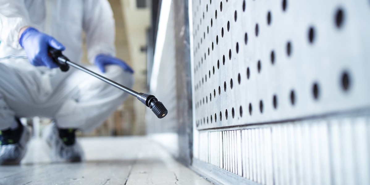 Operatore in tuta bianca di protezione chimica che disinfetta un’area pubblica