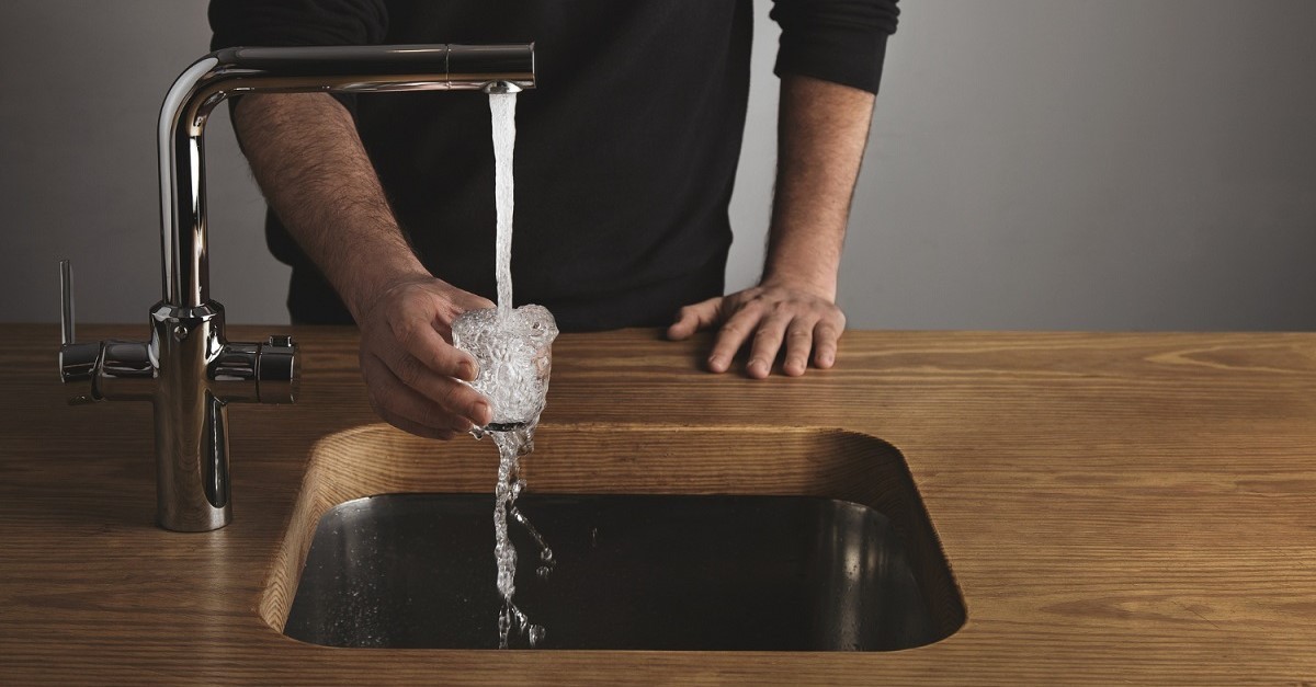 Un uomo versa acqua del rubinetto in un bicchiere