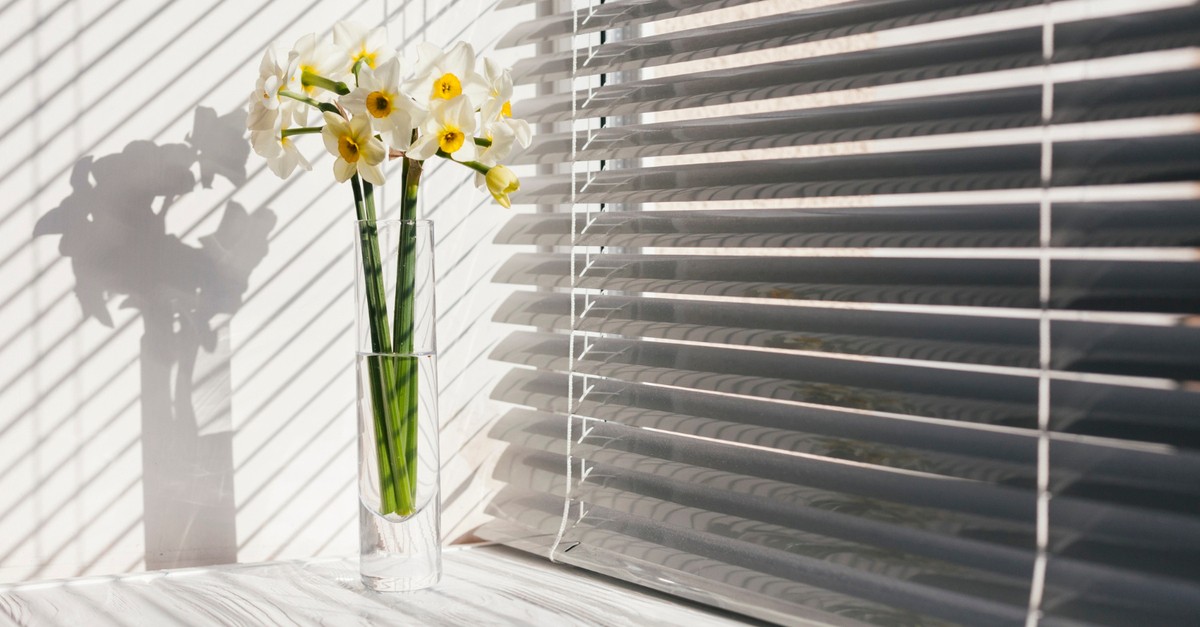 Tapparelle bianche vicino ad un vaso in vetro com fiori gialli