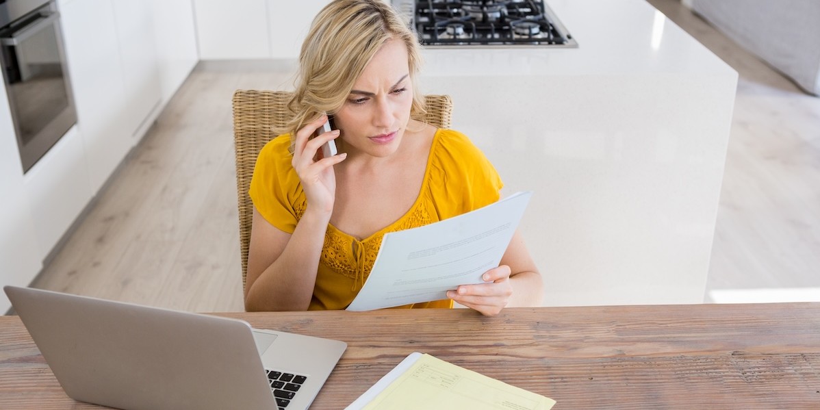 Donna che parla al cellulare in cucina mentre guarda un documento fiscale