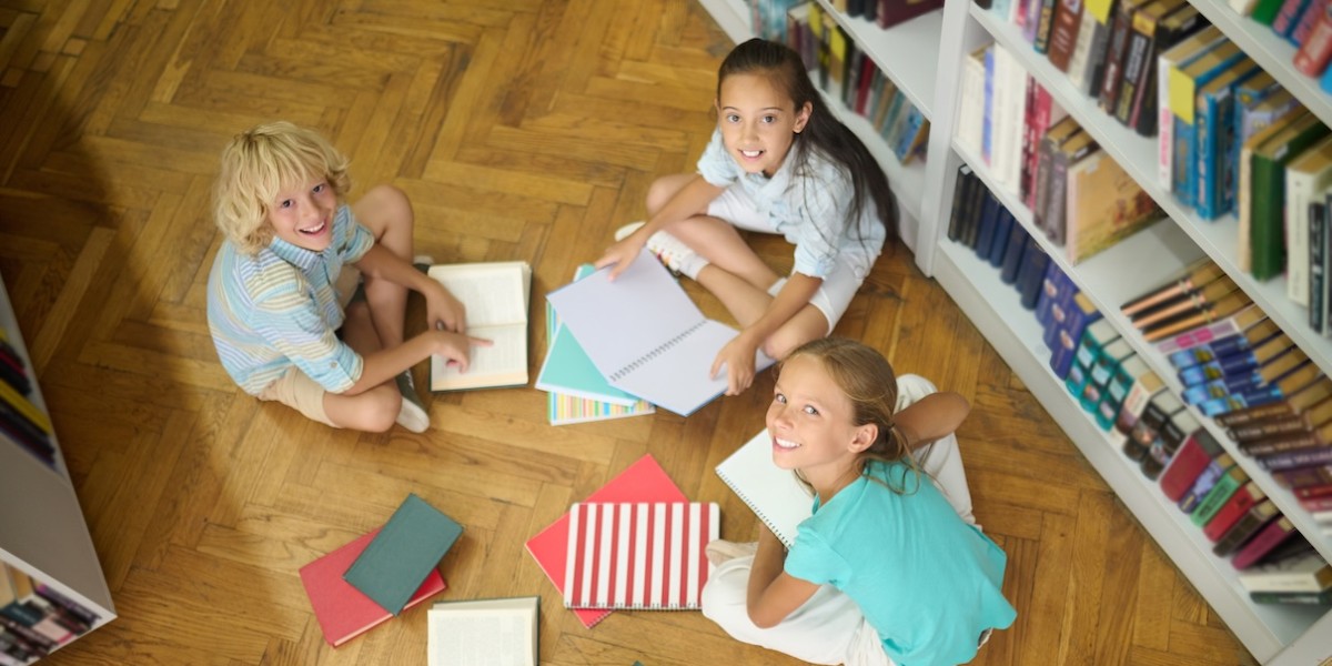 Vista dall'alto di un bambino sorridente e due bambine in età scolare seduti sul pavimento della biblioteca