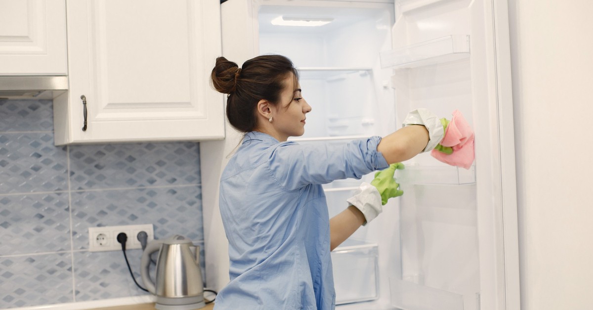 Giovane donna con guanti gialli pulisce il frigo