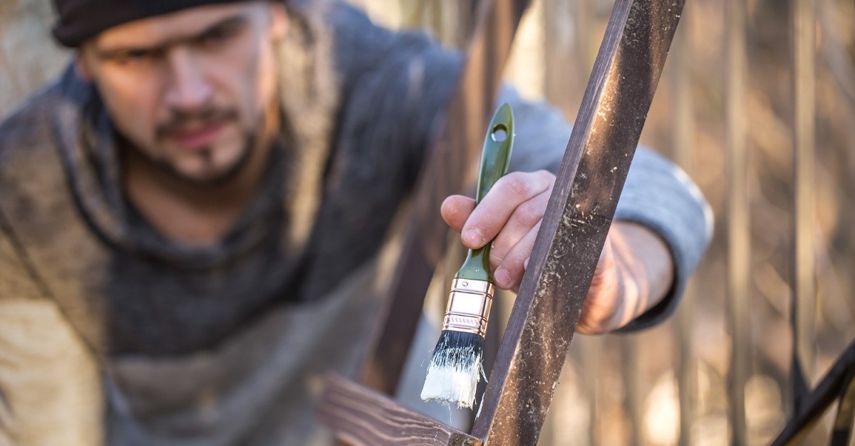 Uomo dipinge di bianco una struttura in legno