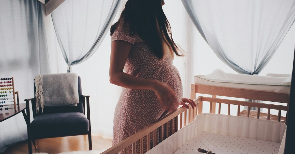 Donna incinta accanto ad un lettino in legno