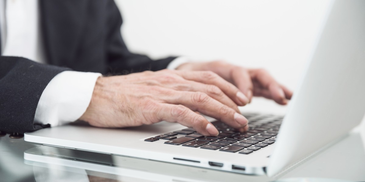 Primo piano di un uomo che scrive al computer portatile su una scrivania di vetro