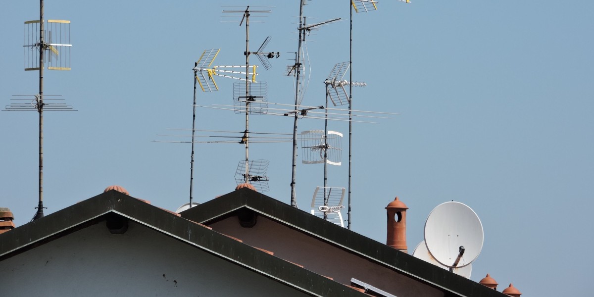 Una raccolta di varie antenne televisive sulla cima di un tetto sotto un cielo blu chiaro in Italia.