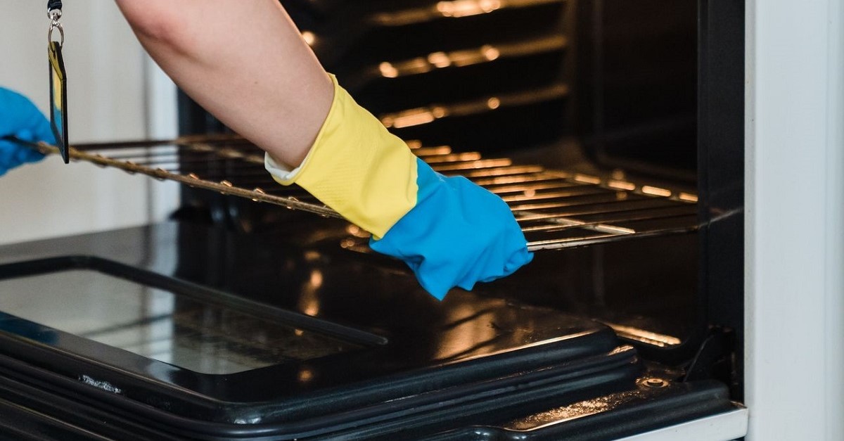 Donna estrae griglia dal forno per pulirlo