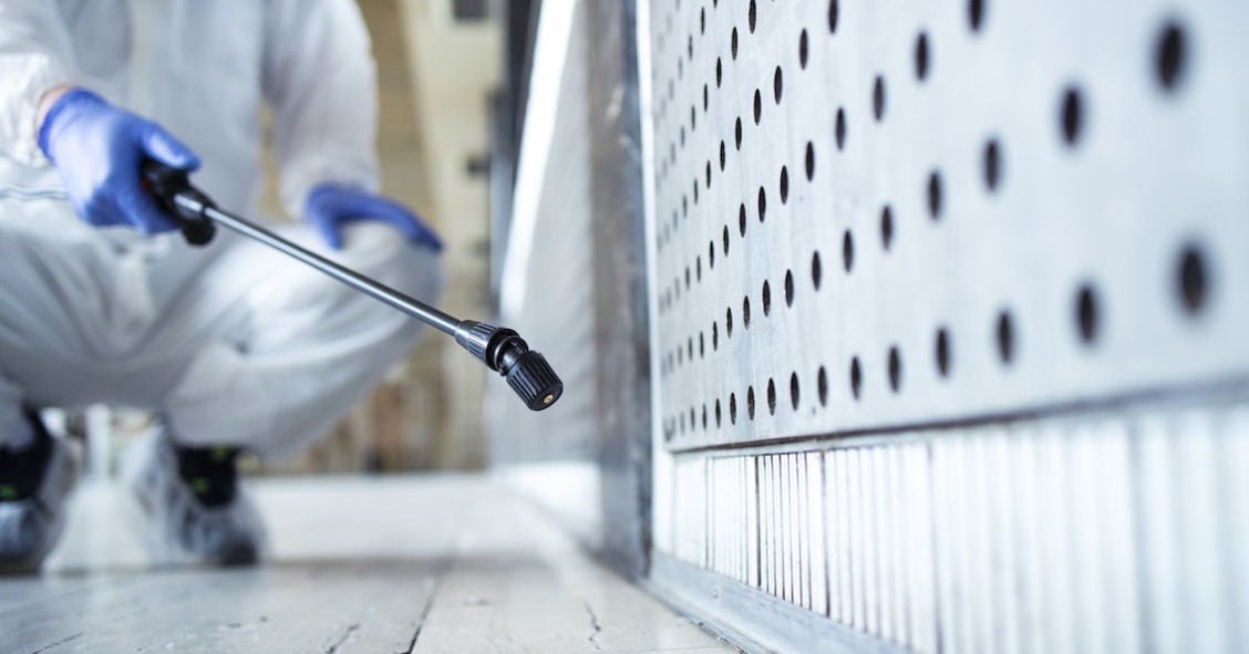 Operatore in tuta bianca di protezione chimica che disinfetta un’area pubblica