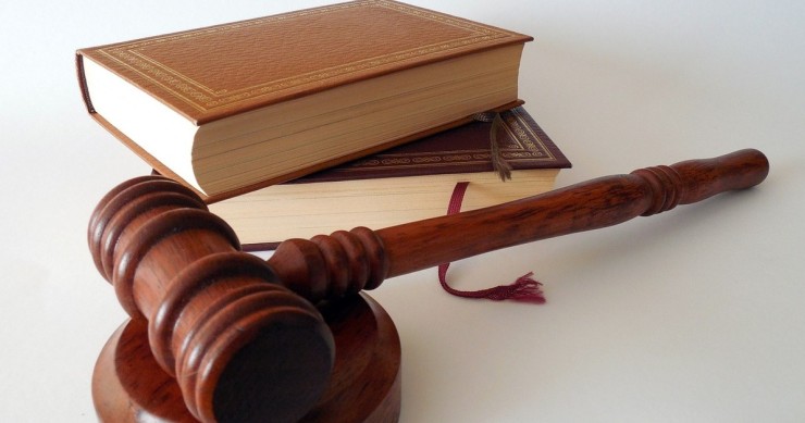 Un martelletto da giudice in legno marrone su un tavolo accanto ad un libro di legge