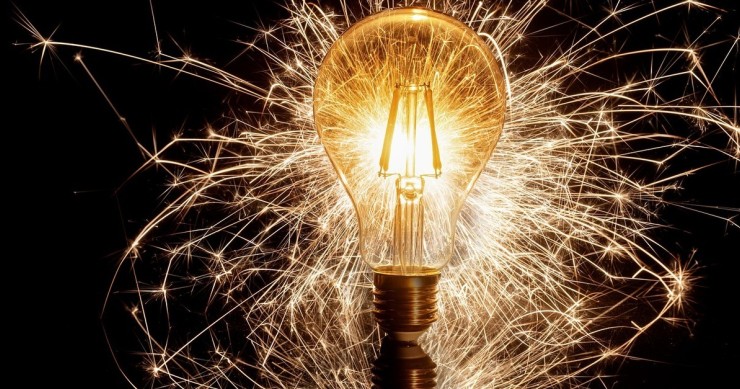 L' immagine di una lampadina accesa circondata da fili luminosi su sfondo nero