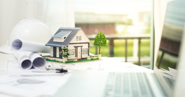 Il modellino di una casa accanto ad un laptop aperto e a dei progetti