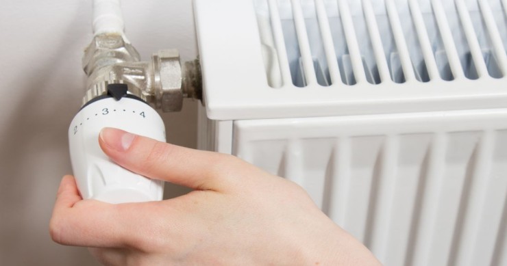 Mano di una persona intenta a ruotare o regolare una moderna valvola termostatica installata su un termosifone