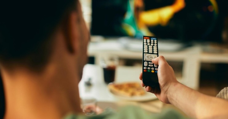 Un uomo guarda la TV col telecomando in mano