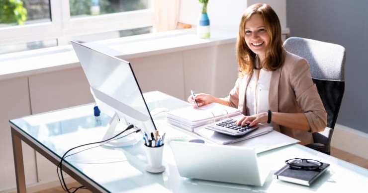 Una professionista seduta a una scrivania in un ufficio moderno intenta a consultare documenti che richiamano pratiche aziendali, bilanci o modelli F24