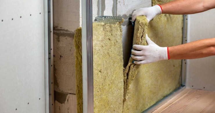 Primo piano delle mani di un operaio edile che applica un pannello isolante termico su una parete