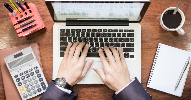 Vista dall'alto delle mani di un uomo d'affari al lavoro su laptop e tablet su una scrivania in legno