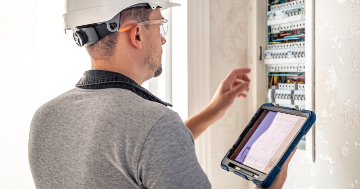 Elettricista lavora su un quadro elettrico con fusibili e utilizza un tablet