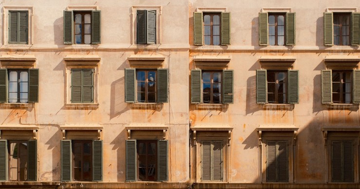Elegante facciata di un edificio storico con finestre con persiane che proiettano ombre nella calda luce del sole.