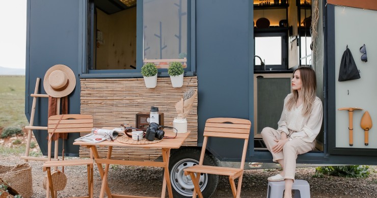 Una donna che si rilassa fuori dalla sua moderna tiny house mobile in un ambiente naturale panoramico.