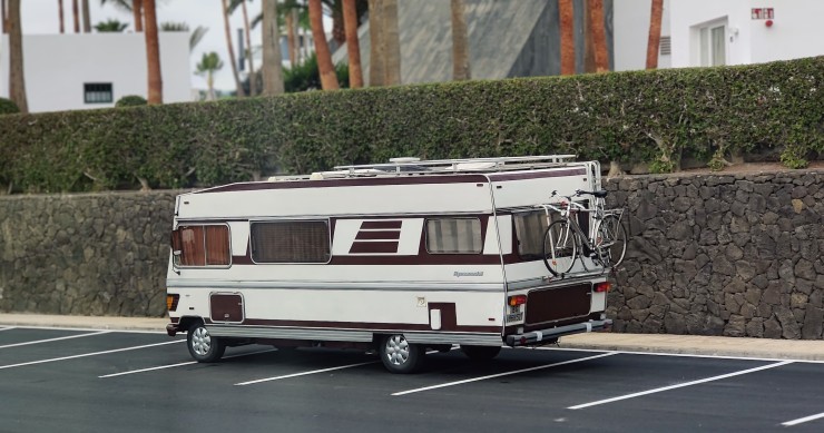 Un camper d'epoca parcheggiato all'aperto vicino a un edificio moderno con palme, a suggerire un mix di avventura e relax.
