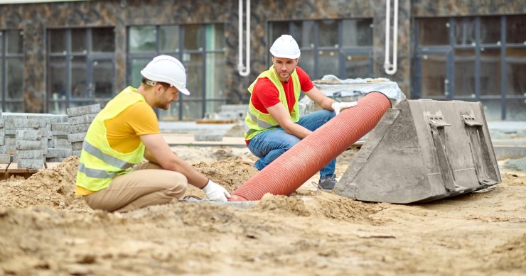 Due uomini accovacciati vicino a un tubo in un cantiere 