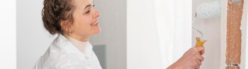 Una donna in camicia bianca dipinge una parete 