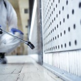 Operatore in tuta bianca di protezione chimica che disinfetta un’area pubblica
