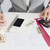 Mani di una persona appoggiate su una scrivania, intenta a fare dei calcoli con una calcolatrice