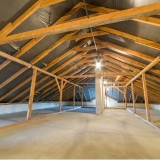 Sottotetto vuoto con travi in legno a vista e tetto spiovente, pulito e luminoso, pronto per la ristrutturazione