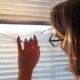 Donna guarda fuori da una finestra con veneziane