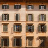 Elegante facciata di un edificio storico con finestre con persiane che proiettano ombre nella calda luce del sole.