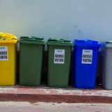 Cinque bidoni di riciclaggio colorati organizzati per la segregazione dei rifiuti in un contesto urbano