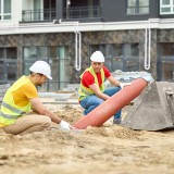 Due uomini accovacciati vicino a un tubo in un cantiere