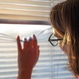 Donna guarda fuori da una finestra con veneziane