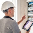 Elettricista lavora su un quadro elettrico con fusibili e utilizza un tablet